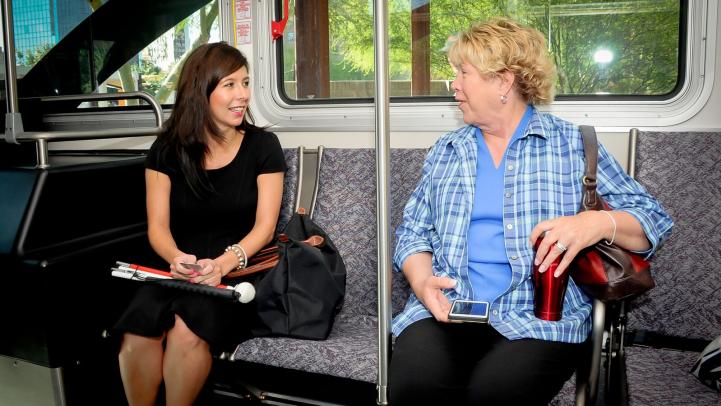 Two riders sit next to each other and talk while on the light rail.