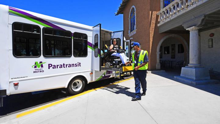 Paratransit rider in wheelchair on vehicle lift helped by operator.